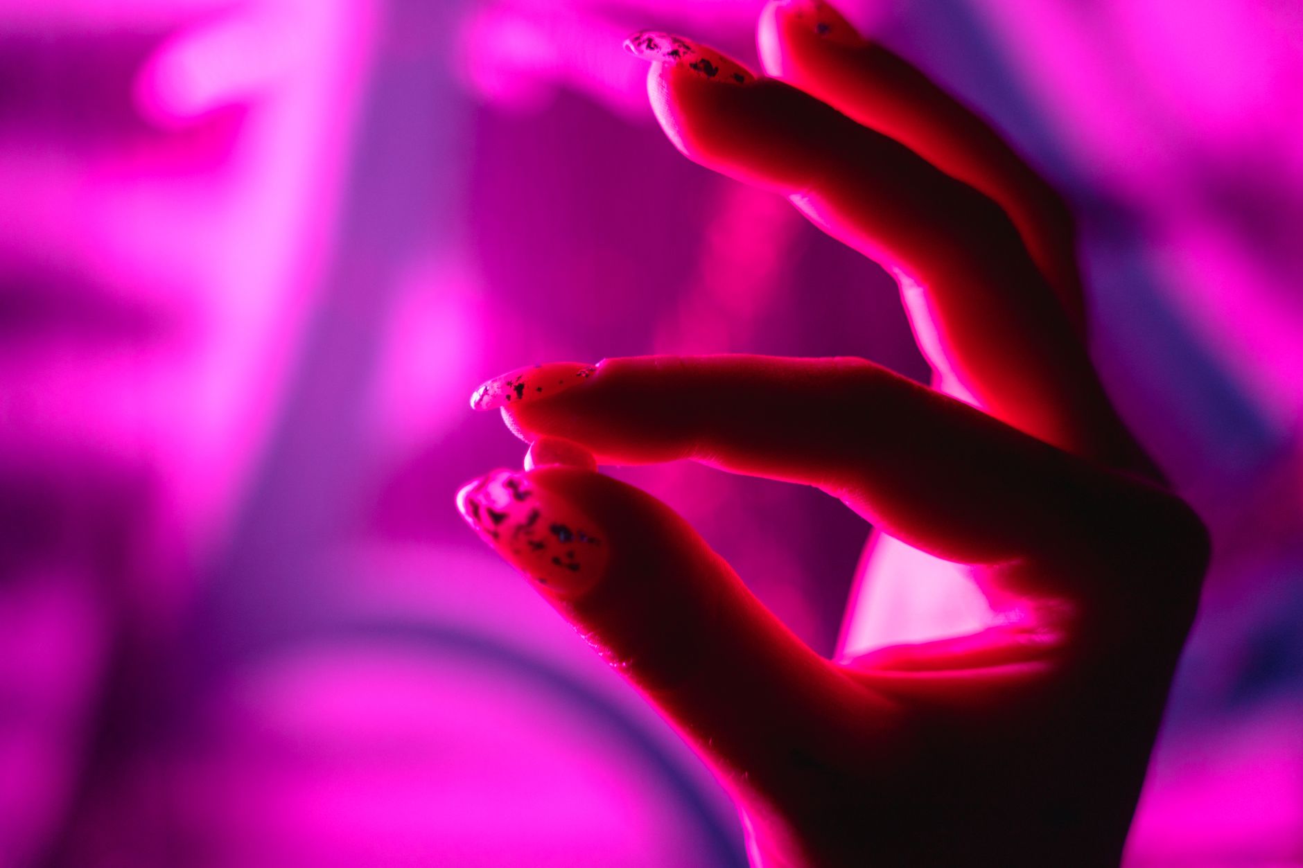 Hand with detailed nail art lit by vivid pink and purple light