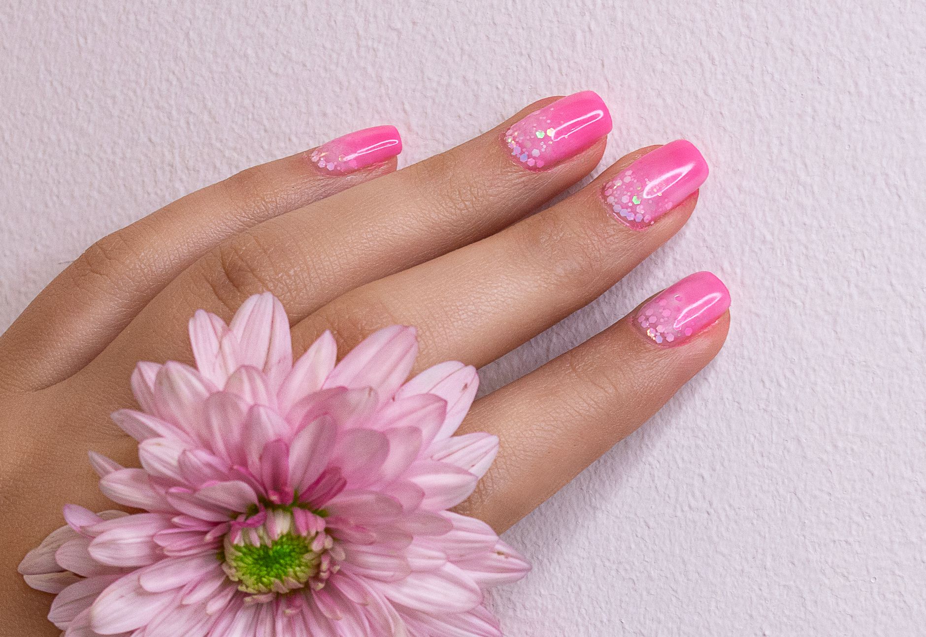 Glossy pink manicure beside a soft pink flower